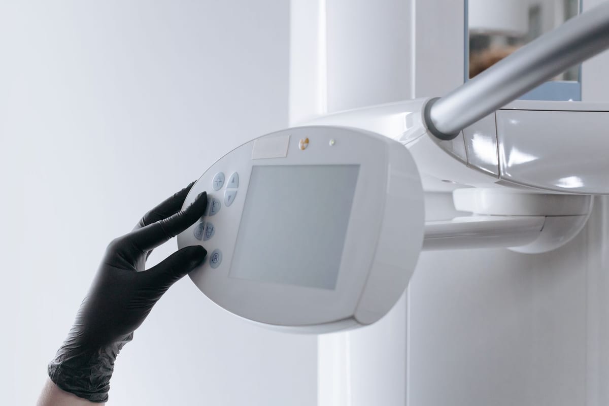 A gloved hand setting the control panel of a dental x-ray unit