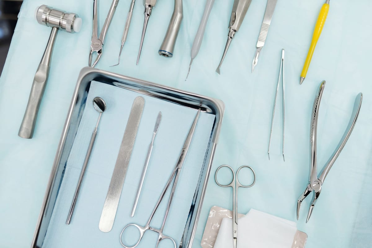 A laid out tray of stainless dental surgery instruments on a sterile drape